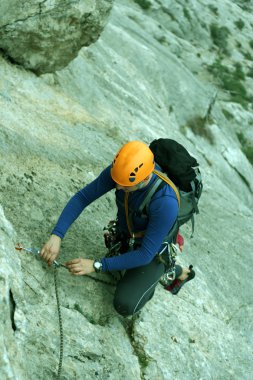 Genç adam arka planında geniş bir vadiyle kireçtaşı bir duvara tırmanıyor.