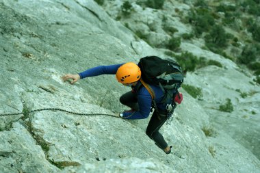 Genç adam arka planında geniş bir vadiyle kireçtaşı bir duvara tırmanıyor.