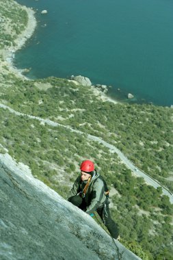 Genç adam arka planında geniş bir vadiyle kireçtaşı bir duvara tırmanıyor.