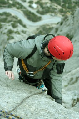 Genç adam arka planında geniş bir vadiyle kireçtaşı bir duvara tırmanıyor.