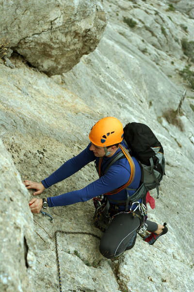 Young man climbing on a limestone wall with wide valley on the background