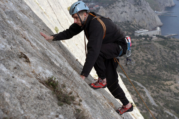 Young man climbing on a limestone wall with wide valley on the background