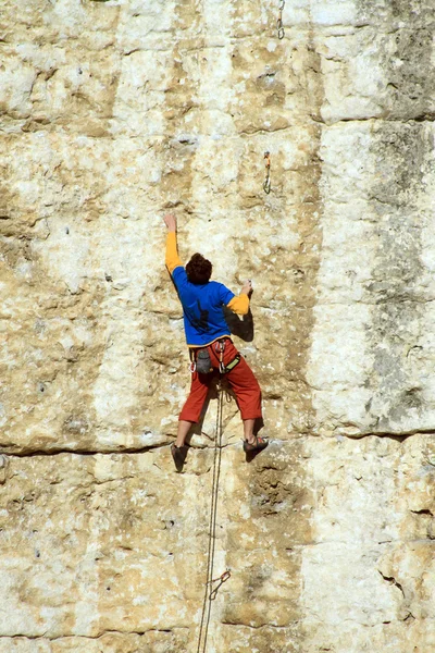 Молодой человек взбирается на известняковую стену с широкой долиной на заднем плане — стоковое фото