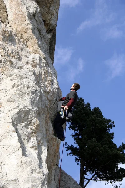 Junger Mann klettert senkrechte Wand mit Talblick im Hintergrund — Stockfoto