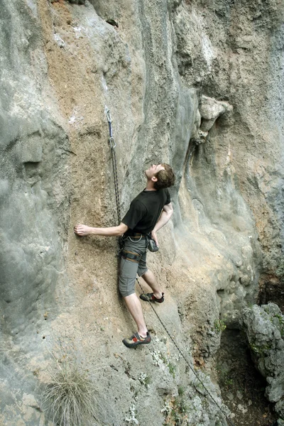 Hombre joven escalando pared vertical con vista al valle en el fondo —  Fotos de Stock