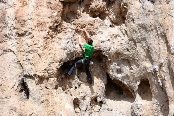 Hombre joven escalando pared vertical con vista al valle en el fondo — Foto de Stock