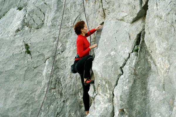 Hombre joven escalando pared vertical con vista al valle en el fondo —  Fotos de Stock