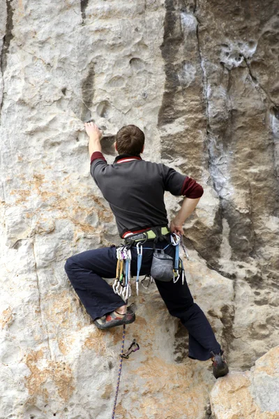 Hombre joven escalando pared vertical con vista al valle en el fondo — Foto de Stock