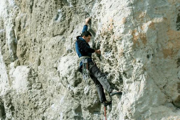 Hombre joven escalando pared vertical con vista al valle en el fondo —  Fotos de Stock