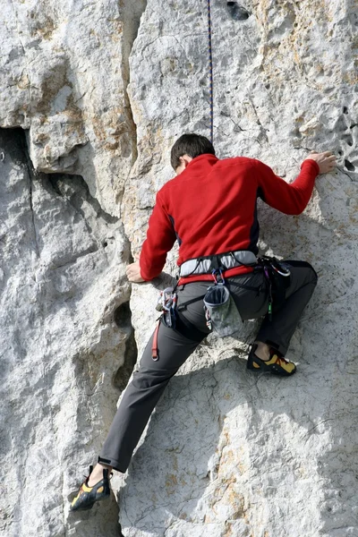 Hombre joven escalando pared vertical con vista al valle en el fondo —  Fotos de Stock