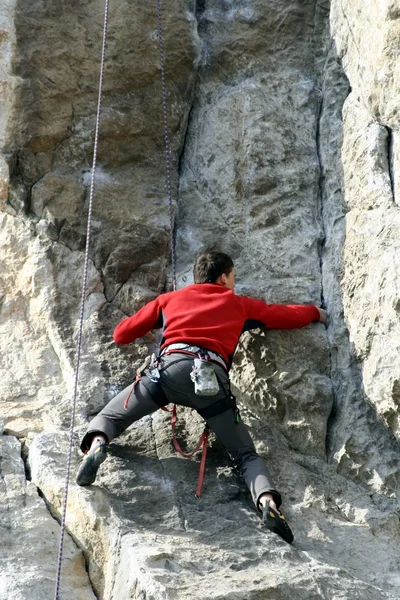 Hombre joven escalando pared vertical con vista al valle en el fondo — Foto de Stock