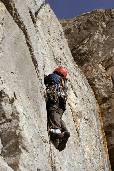 Hombre joven escalando pared vertical con vista al valle en el fondo — Foto de Stock