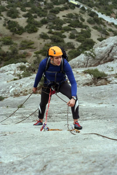 Hombre joven escalando pared vertical con vista al valle en el fondo —  Fotos de Stock