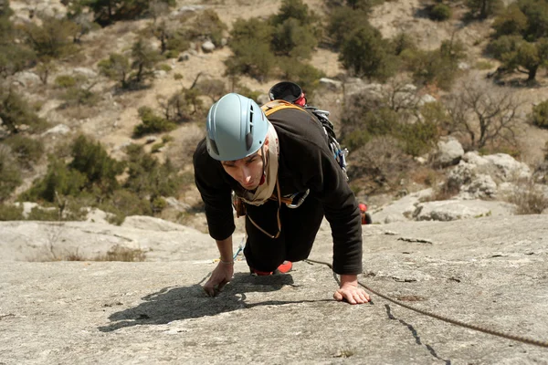 Young man climbing vertical wall with valley view on the background — Stock Photo, Image