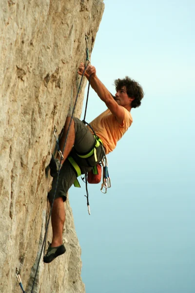 Young man climbing vertical wall with valley view on the background — Stock Photo, Image