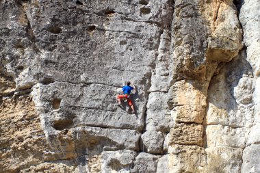 Genç adam arka planında geniş bir vadiyle kireçtaşı bir duvara tırmanıyor.