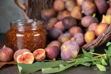 Bir sepet taze incir ve koyu gri arka planda bir kavanoz incir reçeli.