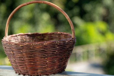 Yeşil yaprakların arka planında klasik hasır sepet.