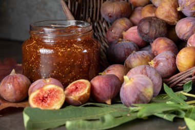 Bir sepet taze incir ve koyu gri arka planda bir kavanoz incir reçeli.