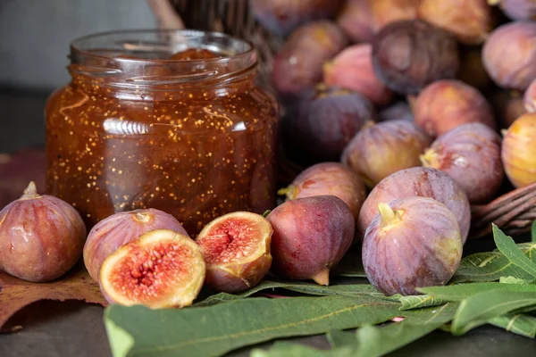 Bir sepet taze incir ve koyu gri arka planda bir kavanoz incir reçeli.