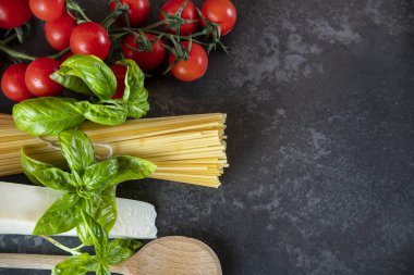 Koyu arkaplanda spagetti, peynir, domates ve fesleğen.
