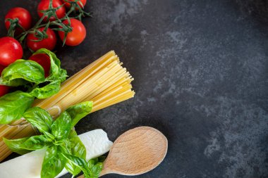 Koyu arkaplanda spagetti, peynir, domates ve fesleğen.