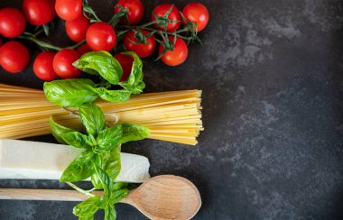 Koyu arkaplanda spagetti, peynir, domates ve fesleğen.