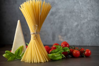 Koyu arkaplanda spagetti, peynir, domates ve fesleğen.