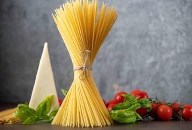 Koyu arkaplanda spagetti, peynir, domates ve fesleğen.