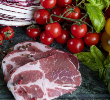 Koyu yeşil mermer tahtada taze et, baharat ve çeşitli sebzeler.