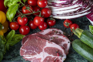 Koyu yeşil mermer tahtada taze et, baharat ve çeşitli sebzeler.