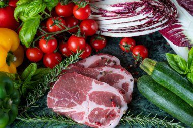 Koyu yeşil mermer tahtada taze et, baharat ve çeşitli sebzeler.