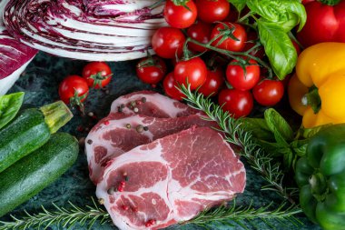 Koyu yeşil mermer tahtada taze et, baharat ve çeşitli sebzeler.