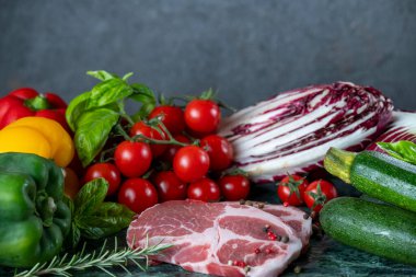 Koyu yeşil mermer tahtada taze et, baharat ve çeşitli sebzeler.