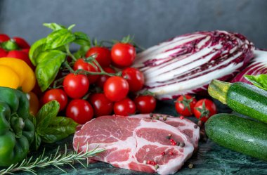 Koyu yeşil mermer tahtada taze et, baharat ve çeşitli sebzeler.