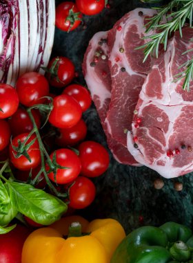 Koyu yeşil mermer tahtada taze et, baharat ve çeşitli sebzeler.