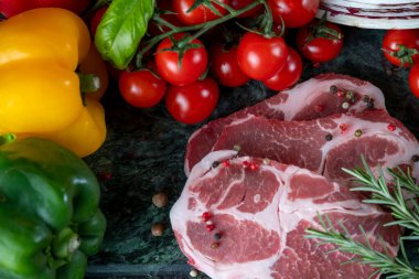 Koyu yeşil mermer tahtada taze et, baharat ve çeşitli sebzeler.