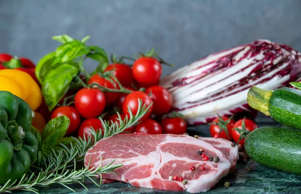 Koyu yeşil mermer tahtada taze et, baharat ve çeşitli sebzeler.