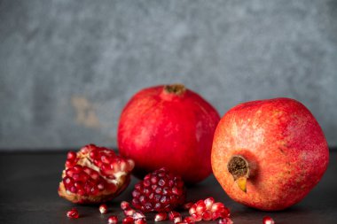 Koyu gri arka planda iki kırmızı nar ve nar tohumu.