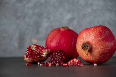 Koyu gri arka planda iki kırmızı nar ve nar tohumu.