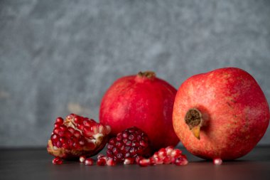 Koyu gri arka planda iki kırmızı nar ve nar tohumu.
