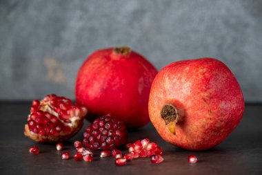 Koyu gri arka planda iki kırmızı nar ve nar tohumu.
