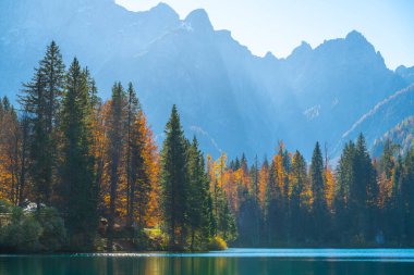 Dağ gölü, sonbahar ağaçları ve güneş ışığındaki güçlü dağlar.