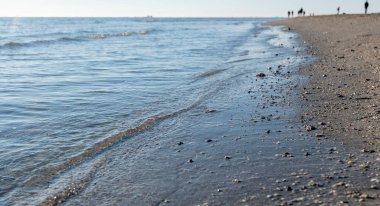 Açık gökyüzüne karşı kumlu sahil ve arka plandaki insanlar