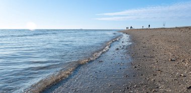 Açık gökyüzüne karşı kumlu sahil ve arka plandaki insanlar