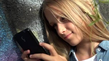 Çocuk parkta akıllı telefonda oynuyor, çocuk akıllı telefonda internete bakıyor, sarışın ergen kız cihazda mesajlar yazıyor.