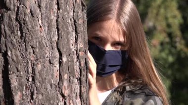 Koronavirüs salgını nedeniyle koruyucu maske takan hasta çocuk, parkta tecrit edilmiş üzgün kız, oynamayan mutsuz genç kız.