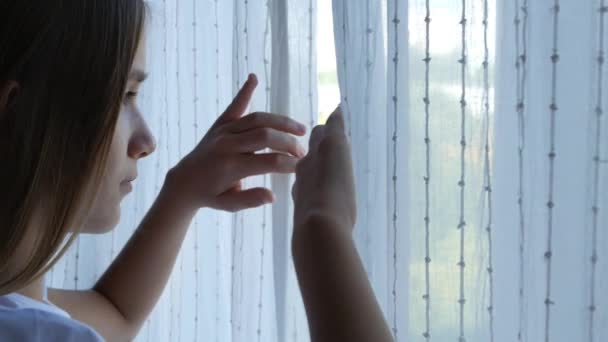 Beteg, elszigetelt gyermek a Coronavirus világjárványban Az ablakfüggöny kinyitása, Boldogtalan lány, aki a szabadban néz az üvegre, Unatkozó kölyök — Stock videók