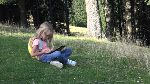 Niño jugando a la tableta en el prado en el camping en las montañas, el niño usa teléfonos inteligentes en el bosque, la niña juega en el dispositivo al aire libre en el parque — Vídeo de stock
