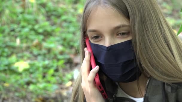 Больная девочка в защитной маске из-за пандемии коронавируса, ребенок разговаривает по смартфону в парке, ребенок общается по смартфону — стоковое видео